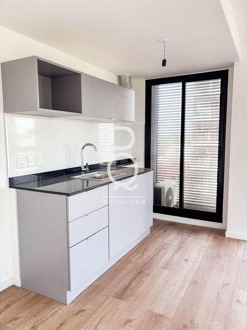 This is a modern kitchen area featuring light gray cabinetry with a dark countertop and a stainless steel sink. The space includes a white tiled backsplash and light wood-look flooring, all in excelle