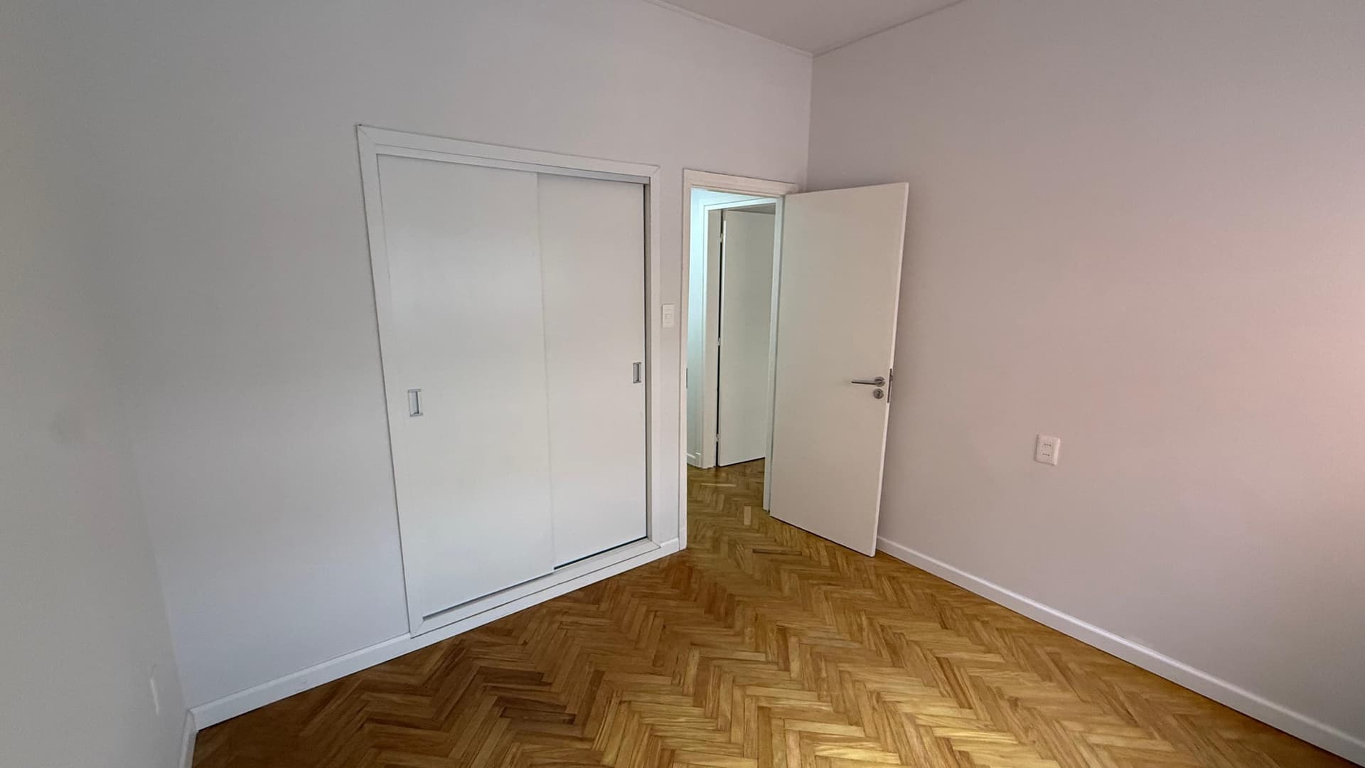 # Bedroom
This bedroom features soft pink walls and herringbone-pattern hardwood flooring in good condition. The space includes a large sliding closet with mirrored doors on the left wall and an additional single door closet on the right, providing ample storage. The room is bright and clean with white trim and appears to be unfurnished and ready for occupancy.