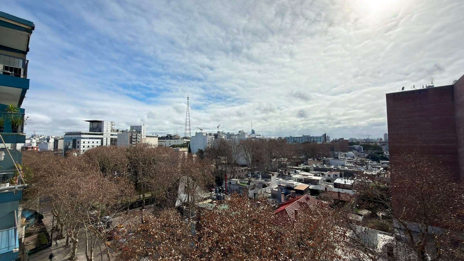 # Property Image Description
**Exterior/City View** - This image captures an expansive urban skyline view from an elevated vantage point, likely from a high-rise residential building. The vista showcases a dense cityscape with mixed architectural styles, including modern office buildings, residential structures, and a distinctive church spire in the distance, with bare trees and rooftops visible throughout the foreground. The property appears to offer excellent panoramic city views with clear sightlines across multiple neighborhoods under partly cloudy skies.