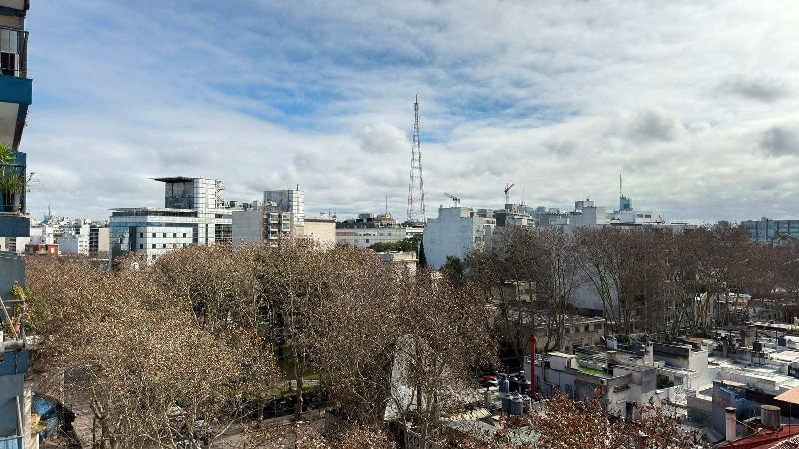 # Property Image Description
**Exterior/Balcony View** - This image showcases an expansive urban cityscape view from a high-rise residential unit, featuring a modern balcony with contemporary teal-colored railings on the left side. The vista captures a vibrant metropolitan skyline with mixed-use buildings, communication towers, and bare deciduous trees in the foreground, under partly cloudy skies. The elevated vantage point offers excellent sightlines across the urban landscape with diverse architectural styles visible throughout the downtown area.