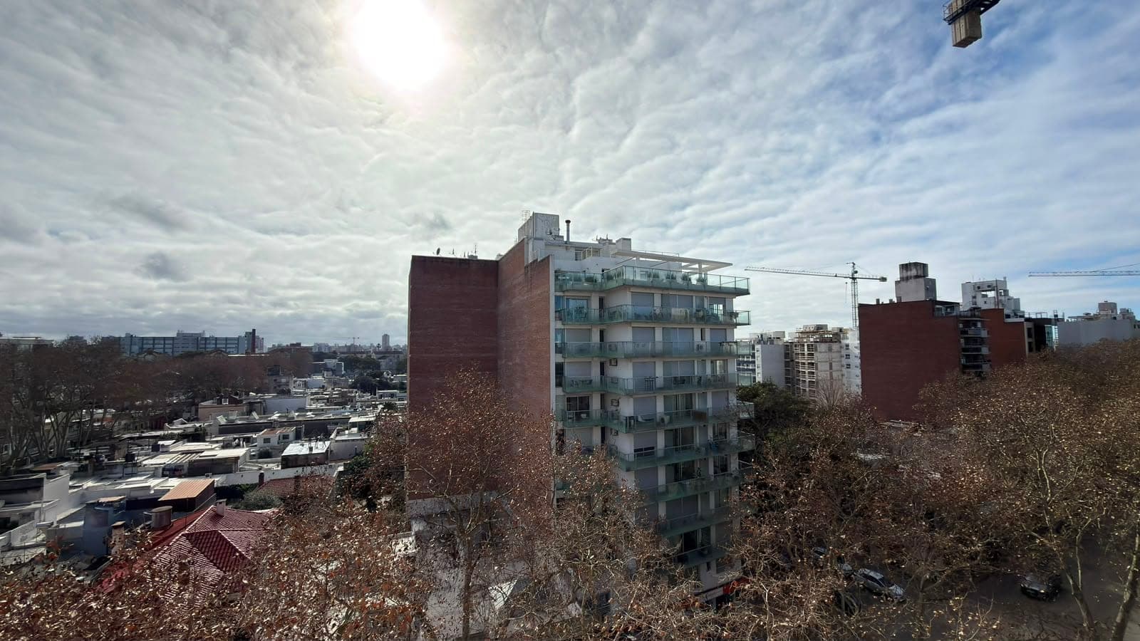 # Property Image Description
**Exterior/Urban View** - This image captures an elevated cityscape view showcasing a dense urban neighborhood with mixed-use residential buildings. The foreground features brick and concrete mid-rise apartment buildings with balconies and modern glass railings, while the background reveals an expansive city skyline with various architectural styles. The scene is characterized by clear daytime lighting under partly cloudy skies, with bare deciduous trees indicating a winter or early spring season, and visible construction cranes suggesting ongoing development in the area.