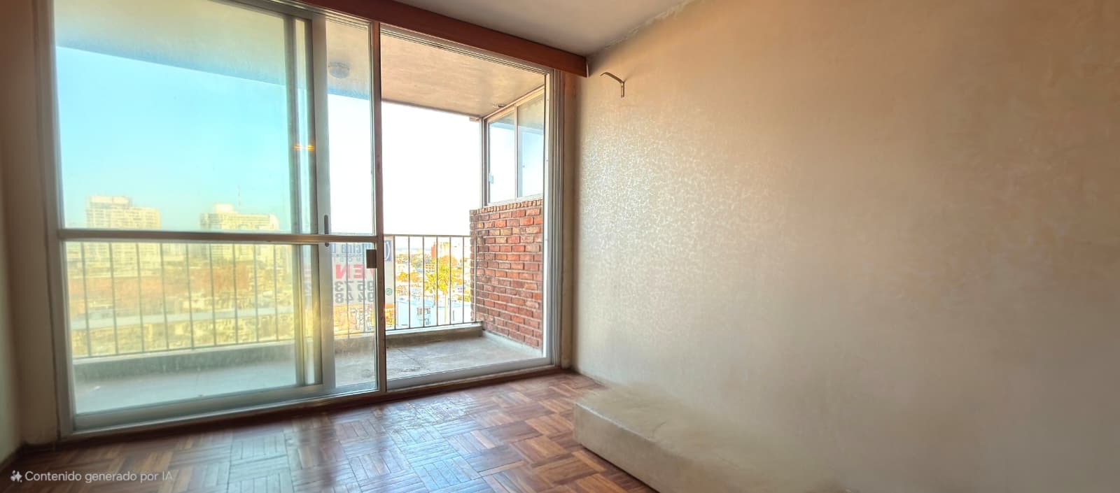 # Property Description
This is a bright bedroom or living space featuring expansive floor-to-ceiling glass doors and windows that open onto a balcony with panoramic city views. The room showcases hardwood parquet flooring in good condition, neutral beige walls, and abundant natural light throughout. Notable features include a brick accent wall visible from the balcony, metal railings, and modern sliding glass door systems that provide excellent ventilation and an open feel to the space.
WATERMARK: Contenido generado por IA