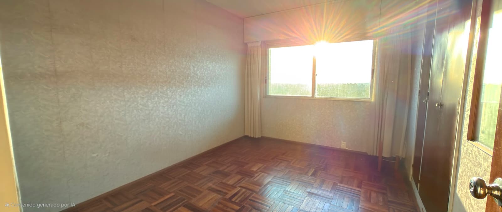 This is a spacious bedroom featuring a parquet wood floor in a herringbone pattern and neutral beige/cream colored walls. The room is flooded with natural light from large windows with cream curtains that offer views of green landscaping outside, and includes a mirrored wardrobe on the right side. The space appears clean and well-maintained, with good proportions suitable for a master or secondary bedroom.
WATERMARK: Generated by IA