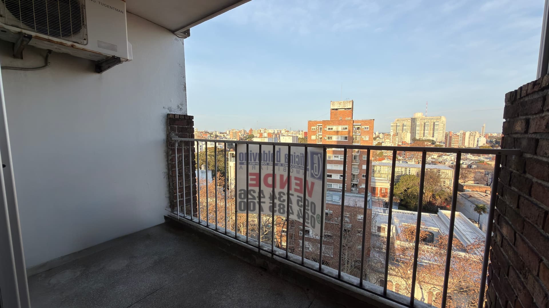 # Property Description
This is a high-rise balcony/terrace offering expansive panoramic city views of an urban skyline with numerous residential and commercial buildings. The space features a black metal railing, concrete flooring, and an air conditioning unit mounted on the white exterior wall. The balcony provides excellent natural light and unobstructed vistas across the cityscape, making it an ideal outdoor extension for a residential unit.
WATERMARK: EDLEN