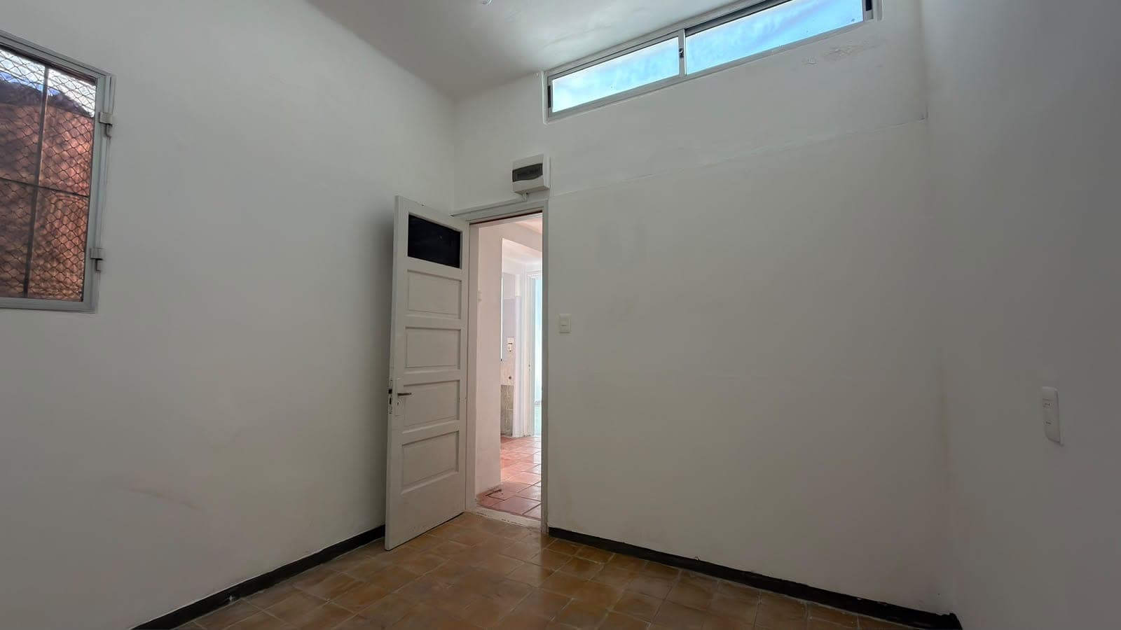 # Property Image Description
This is a modern, minimalist interior space featuring clean white walls and excellent natural lighting from a transom window above. The room includes a white panel door with an integrated display screen, dark tile flooring with a black border detail, and a wall-mounted air conditioning unit, suggesting this may be a bedroom, office, or utility space. The bright, airy design and contemporary finishes indicate a well-maintained property with modern amenities.
